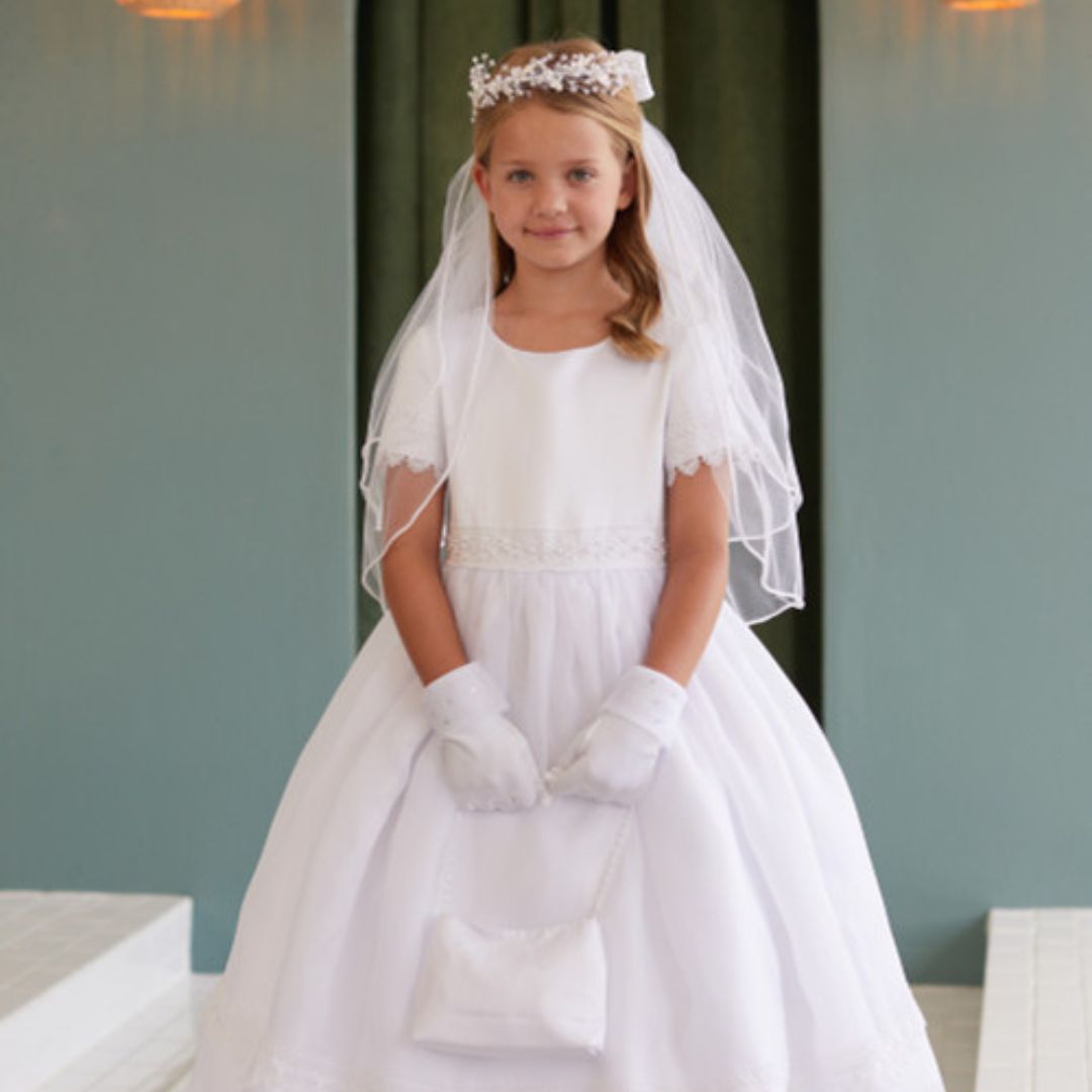 Girl in a white communion dress with a veil, gloves, and a purse